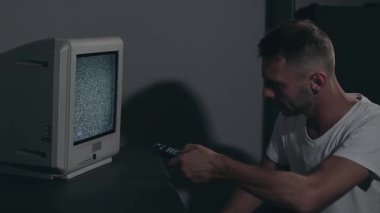 Kırık Televizyon veya TV Propagandası. Zihin Kontrolü - Beyaz tişörtlü Zombi Karanlık Oda 'daki Eski TV kanallarını değiştirdi. TV Sinyal Arama. Ekrandaki bozulma. Ortalama Yakın Çekim, Film Tanesi