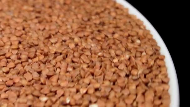 Dry Uncooked Brown Buckwheat Groats White Plate Rotating Black Background — Vídeo de stock