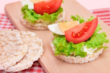 Domatesli Rice Cake Sandviç, Tahta Kesme Kurulunda Marul ve Yumurta. Kolay Kahvaltı 'da. Diyet yemek. Hızlı ve sağlıklı sandviçler. Lezzetli dolgulu kızarmış ekmek. Sağlıklı Beslenme Atıştırması