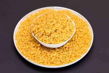 Beyaz Tabakta pişmemiş Chifferi Rigati Pasta Siyah Arkaplanda. Şişman ve Sağlıksız Yemek. Dağıtılmış klasik kuru makarna. İtalyan Kültür ve Mutfağı. Çiğ Makarna