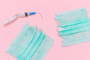 Aşı Karşıtı Hareket ve Maske Karşıtı Konsept - Kırık Tıbbi Şırınga ve Pembe Arkaplanda Yeşil Yırtık Tıbbi Maske. Salgın ve Kilitlenme Sonu - Üst Görünüm, Düz Yat