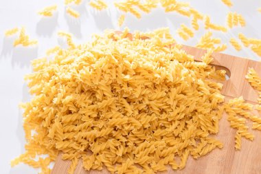 Tahta tahtada ve beyaz masada pişmemiş Fusilli Makarna. Çiğ ve kuru makarna. Şişman ve Sağlıksız Yemekler