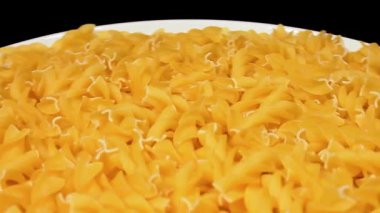 Beyaz Tabakta pişmemiş Fusilli Makarna Siyah Arkaplan 'a karşı dönüyor. Şişman ve Sağlıksız Yemek. Kuru Spiral makarna. İtalyan Kültür ve Mutfağı. Çiğ Altın Makarna