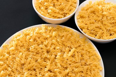 Pişmemiş Fusilli Makarna Siyah Arkaplanda Beyaz Tabakta Yatıyor. Çiğ ve kuru makarna. Sağlıksız ve şişman yiyecekler
