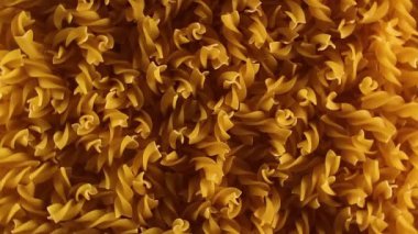 Pişmemiş Fusilli Makarna - Üst Manzara. Şişman ve Sağlıksız Yemek. Kuru Spiral Makarna, Yavaşça Dönen Arkaplan. İtalyan Kültür ve Mutfağı. Çiğ Altın Makarna deseni. Sol Döndürme, Alçak Anahtarlı Işık