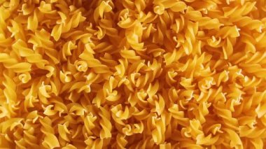 Pişmemiş Fusilli Makarna - Üst Manzara. Şişman ve Sağlıksız Yemek. Kuru Spiral Makarna, Yavaşça Dönen Arkaplan. İtalyan Kültür ve Mutfağı. Çiğ Altın Makarna deseni. Sol Döndürme, Alçak Anahtarlı Işık
