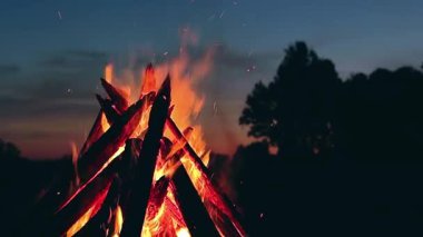 Big Burning Campfire in Early Morning or Evening against the Blue Sky. Wood on Fire. Flying Sparks. Travel and Tourism Concept. Giant Flaming Bonfire at Summer - Static Shot, Slow Motion