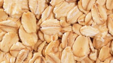 Yulaf Gevreği Arkaplanı Yavaşça Sağa Dönüyor - Üst Manzara, Yakın Çekim. Dağıtılmış Kuru Yulaf Gevreği. Sağlıklı Kahvaltı ve Beslenme Malzemeleri