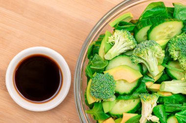 Fresh Green Salad of Avocado, Broccoli, Spinach and Cucumber for Detox with Soy Sauce on Wooden Cutting Board. Vegan Salad. Vegetarian Culture. Raw Food. Healthy Eating and Vegetable Diet clipart