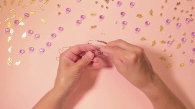 El yapımı Mücevher. Beyaz Tişörtlü Beyaz Avrupalı Kadın Pembe Masa 'da El yapımı Bijouterie, Boncuk ve Bilezik Yapıyor. Sanatçılar İş Yeri - Üst Görünüm, Sabit Çekim