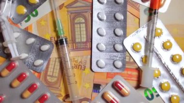 Enflasyon. Pahalı bir ilaç. Yüksek Sağlık Hizmetleri Maliyeti. Global İlaç Endüstrisi ve Tıbbi Ürünler. Elli Avro Banknotunda Farklı Haplar ve Şırıngalar - Üst Görünüm, Yavaş Dönüşüm