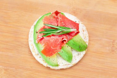 Taze Avokado, Jamon ve Rosemary 'li Rice Cake Sandviçi Bambu Kesme Kurulunda. Kolay Kahvaltı 'da. Diyet yemek. Hızlı ve sağlıklı sandviçler. Lezzetli dolgulu kızarmış ekmek. Sağlıklı Beslenme Atıştırması