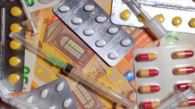 Enflasyon. Pahalı bir ilaç. Yüksek Sağlık Hizmetleri Maliyeti. Global İlaç Endüstrisi ve Tıbbi Ürünler. Elli Avro Banknotunda Farklı İlaç ve Şırıngalar - Üst Görünüm, Yavaş Dönüşüm Sağı
