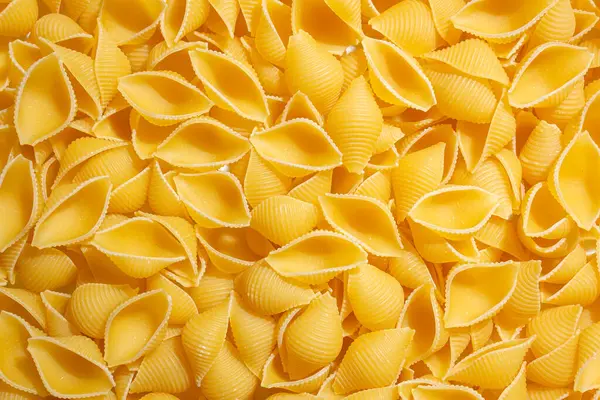 Pişmemiş Conchiglie Pasta: Konchiglie Macaroni 'nin Mutfak Tuvali, Gurme Yemekleri İçin Canlı ve Dokulu Bir Arkaplan Oluşturuyor. Kuru makarna. Raw Macaroni - Top View, Düz Yat