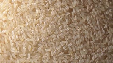 Dry Uncooked Parboiled Rice Background Rotating Right - Top View, Low Key Light. Scattered Raw Long Grain Rice. Asian Cuisine and Culture. Healthy Eating Ingredients. Diet Food