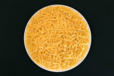 Pişmemiş Fusilli Makarna Siyah Arkaplanda Beyaz Tabakta Yatıyor. Çiğ ve kuru makarna. Sağlıksız ve Yağlı Gıda - Üst Görünüm