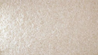 Kuru, pişmemiş, beyaz pirinç arka planı yavaşça sola doğru dönüyor. Çiğ Uzun Taneli Pirinç. Asya mutfağı ve kültürü. Sağlıklı beslenme malzemeleri. Diyet Yemekler
