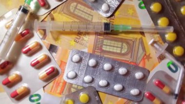 Enflasyon. Pahalı bir ilaç. Yüksek Sağlık Hizmetleri Maliyeti. Global İlaç Endüstrisi ve Tıbbi Ürünler. Elli Avro Banknotunda Farklı İlaç ve Şırıngalar - Üst Görünüm, Yavaş Dönüşüm Sağı