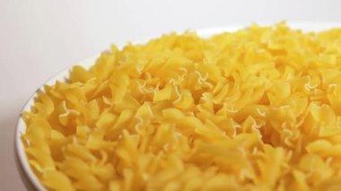 Beyaz Plaka 'da pişmemiş Fusilli Makarna Beyaz Arkaplan' a karşı dönüyor. Şişman ve Sağlıksız Yemek. Kuru Spiral makarna. İtalyan Kültür ve Mutfağı. Çiğ Altın Makarna