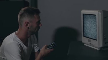 Kırık Televizyon veya TV Propagandası. Zihin Kontrolü - Beyaz tişörtlü Zombi Karanlık Oda 'daki Eski TV kanallarını değiştirdi. TV Sinyal Arama. Ekrandaki bozulma. Ortalama Yakın Çekim, Film Tanesi