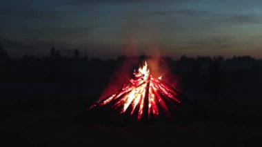 Big Burning Campfire in Early Morning or Evening against the Blue Sky. Wood on Fire. Flying Sparks. Travel and Tourism Concept. Giant Flaming Bonfire at Summer - Static Shot, Slow Motion