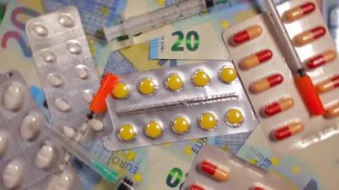 Enflasyon. Pahalı bir ilaç. Yüksek Sağlık Hizmetleri Maliyeti. Global İlaç Endüstrisi ve Tıbbi Ürünler. Yirmi Avro Banknotlarında Farklı İlaç ve Şırıngalar - Üst Görünüm, Sol Rotasyon