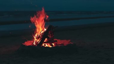 Dalgalı Deniz 'e karşı sahilde şenlik ateşi ya da Bulutlu Bir Zamanda Gece Okyanusu. Kum tepesinde yanan kamp ateşi. Ateşe odun. Şenlik Ateşi için yer. Deniz kenarındaki ateş çukuru. Sinyal Ateşi - Sabit Çekim, Yavaş Hareket