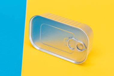 Bölünmüş mavi ve sarı arka plandaki teneke kutu. Konserve yiyecekler. Güvenli ve uzun vadeli yiyecek depolama için alüminyum kutu. Çelik Mühürlü Yiyecek Depolama Kutusu