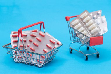 İlaç almak için. Uyuşturucu Bağımlılığı Konsepti: Mavi Arkaplan 'daki alışveriş arabasında haplar ve kapsüller. Global İlaç Endüstrisi ve Büyük İlaç. İlaç Ürünleri Siparişi