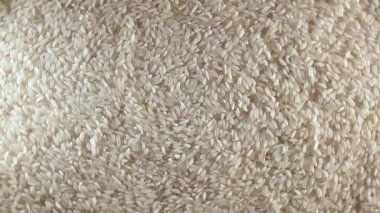 Dry Uncooked White Rice Background Slowly Rotating Right - Top View, Low Key Light. Scattered Raw Long Grain Rice. Asian Cuisine and Culture. Healthy Eating Ingredients. Diet Food