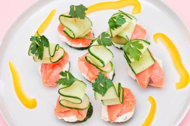 Taze somonlu kanepeler, salatalık ve krem peynirli beyaz tabak. Kolay Kahvaltı 'da. Diyet yemek. Hızlı ve sağlıklı sandviçler. Lezzetli Doldurulmuş Sağlıklı Atıştırmalıklar