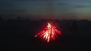 Big Burning Campfire in Early Morning or Evening against the Blue Sky. Wood on Fire. Flying Sparks. Travel and Tourism Concept. Giant Flaming Bonfire at Summer - Static Shot, Slow Motion