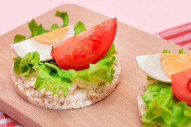 Domatesli Rice Cake Sandviç, Tahta Kesme Kurulunda Marul ve Yumurta. Kolay Kahvaltı 'da. Diyet yemek. Hızlı ve sağlıklı sandviçler. Lezzetli dolgulu kızarmış ekmek. Sağlıklı Beslenme Atıştırması