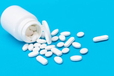 Küresel İlaç Endüstrisi ve İlaç Ürünleri - İlaç Konteynırından Dağılmış Beyaz Haplar veya Tabletler, Mavi Arkaplanda Yatanlar