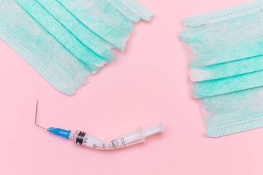 Aşı Karşıtı Hareket ve Maske Karşıtı Konsept - Kırık Tıbbi Şırınga ve Pembe Arkaplanda Yeşil Yırtık Tıbbi Maske. Salgın ve Kilitlenme Sonu - Üst Görünüm, Düz Yat