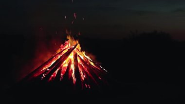 Big Burning Campfire at Summer Night against the Blue Sky. Wood on Fire. Flying Sparks. Travel and Tourism Concept. Giant Flaming Bonfire - Static Shot, Slow Motion