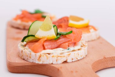 Tahta kesim tahtasında taze somon, salatalık, limon ve yeşillikli pirinç keki sandviçi. Diyet yemek. Hızlı ve sağlıklı sandviçler. Taze dolgulu çıtır ekmek. Sağlıklı Beslenme Atıştırmaları