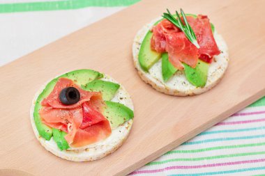 Tahta Kesme Kurulu 'nda Avocado, Jamon, Zeytin ve Rosemary ile Rice Cake Sandviçi. Kolay Kahvaltı 'da. Hızlı ve sağlıklı sandviçler. Lezzetli dolgulu kızarmış ekmek. Sağlıklı Beslenme Atıştırması