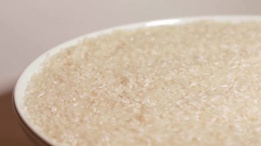 Dry Uncooked White Rice on White Plate Rotating against White Background. Scattered Raw Long Grain Rice. Asian Cuisine and Culture. Healthy Eating Ingredients. Diet Food