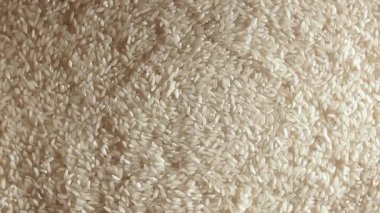 Dry Uncooked White Rice Background Slowly Rotating Right - Top View, Low Key Light. Scattered Raw Long Grain Rice. Asian Cuisine and Culture. Healthy Eating Ingredients. Diet Food