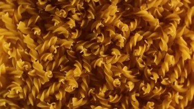Pişmemiş Fusilli Makarna - Üst Görünüm, Düşük Anahtar Işığı. Şişman ve Sağlıksız Yemek. Kuru Spiral makarna, döner arka plan. İtalyan Kültür ve Mutfağı. Çiğ Altın Makarna deseni. Sağ Çevirme