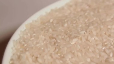 Dry Uncooked White Rice on White Plate Rotating against White Background. Scattered Raw Long Grain Rice. Asian Cuisine and Culture. Healthy Eating Ingredients. Diet Food
