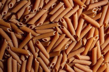 Pişmemiş tam tahıllı Penne Rigate Makarnası: Bir tam buğday Makarnası Mutfak Kanvası, Gurme Aşçılığı İçin Canlı ve Dokulu Bir Arkaplan Oluşturma. Tam Tahıllı Kuru Makarna. Tam buğday hamurlu makarna.