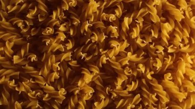 Pişmemiş Fusilli Makarna - Üst Görünüm, Düşük Anahtar Işığı. Şişman ve Sağlıksız Yemek. Kuru Spiral Makarna, Yavaşça Dönen Arkaplan. İtalyan Kültür ve Mutfağı. Çiğ Altın Makarna deseni. Sağ Çevirme