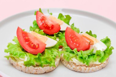 Domatesli pirinç keki sandviç, beyaz tabakta marul ve yumurta. Kolay Kahvaltı 'da. Diyet yemek. Hızlı ve sağlıklı sandviçler. Lezzetli dolgulu kızarmış ekmek. Sağlıklı Beslenme Atıştırması