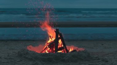 Dalgalı Deniz 'e karşı sahilde şenlik ateşi ya da Bulutlu Bir Zamanda Akşam' da Okyanus. Kum tepesinde yanan kamp ateşi. Ateşe odun. Şenlik Ateşi için yer. Deniz kenarındaki ateş çukuru. Sinyal Ateşi - Sabit Çekim, Yavaş Hareket