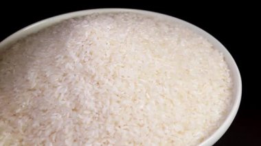 Dry Uncooked White Rice Heap on White Plate Rotating against Black Background. A Pile of Raw Long Grain Rice. Asian Cuisine and Culture. Healthy Eating Ingredients. Diet Food