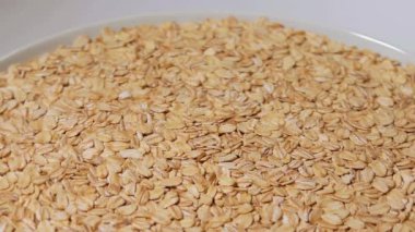 Pişmemiş Yulaf Gevreği Beyaz Plaka 'da Beyaz Arkaplan' a karşı dönüyor. Dağıtılmış Kuru ve Çiğ Yulaf Gevreği. Sağlıklı Kahvaltı ve Beslenme Malzemeleri