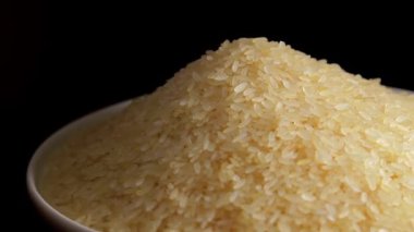 Dry Uncooked Parboiled Rice Heap Rotating against Black Background. A Pile of Raw Long Grain Rice. Asian Cuisine and Culture. Healthy Eating Ingredients. Diet Food