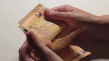 Elde Para Saymak. Avrupa Birliği Parası. Beyaz Kadın Beyaz Masa 'da 50 Euro' luk banknotlar sayıyor. Turuncu Kağıt Nakit. Elde Elli Euro. Gelir, Tasarruf ve Harcama Konsepti